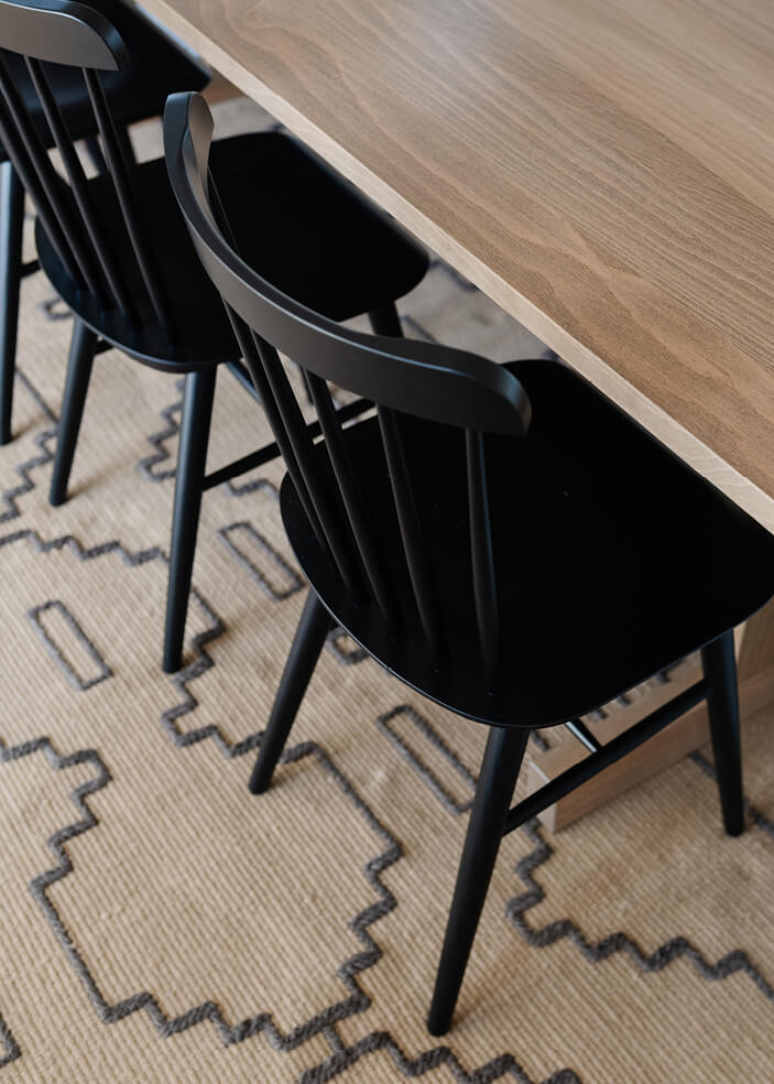 Coastal dining room with a geometric rug, natural wood table, and black chairs in an Edgartown home by a Cape Cod interior designer.