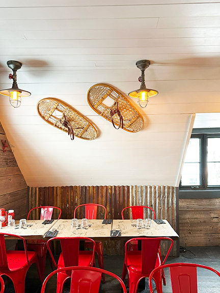 Mont Tremblant restaurant with corrugated metal siding, reclaimed wood panels, shiplap ceilings, red metal chairs, and vintage snowshoes decor.