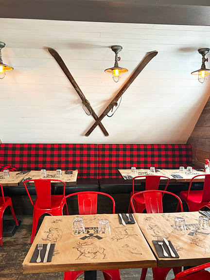 Travel to Mont Tremblant to see a restaurant with red buffalo check, black leather banquette, reclaimed wood, and vintage skis on the ceiling.