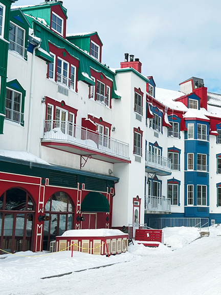 Travel to Mont Tremblant to see bright architecture with a green roof, red accents, and blue siding standing out against snowy slopes.