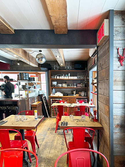 Travel to Mont Tremblant to experience a cozy restaurant with wood floors, reclaimed walls, exposed beams, and red metal chairs.
