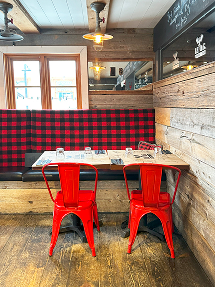 Cozy restaurant in Mont Tremblant with reclaimed wood walls, red buffalo check fabric, black leather banquette, and industrial lighting.
