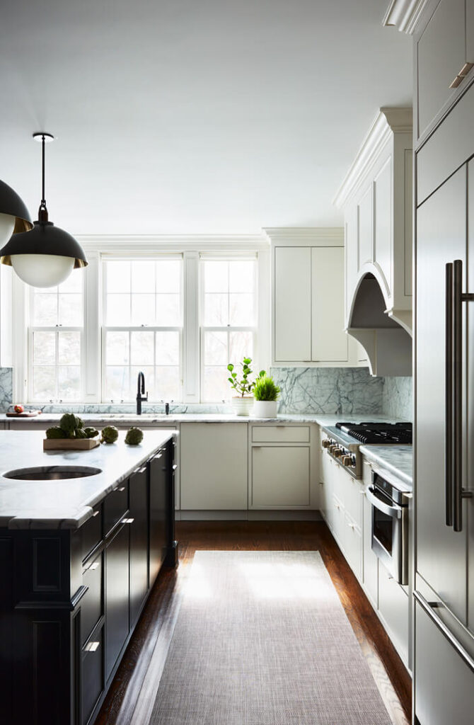 A modern Concord kitchen with slab cabinet doors, metal edge pulls, a black island, and sleek Allied Maker lighting in a historic home.