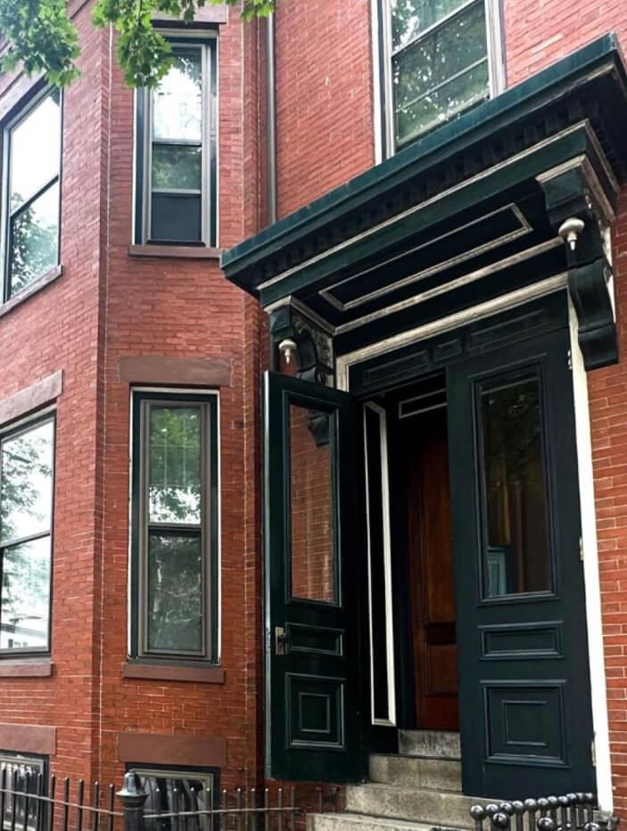 Boston brownstone renovation featuring iconic brick exteriors, a grand 'Essex Green' pediment, intricate corbels, and original green doors with vintage hardware.