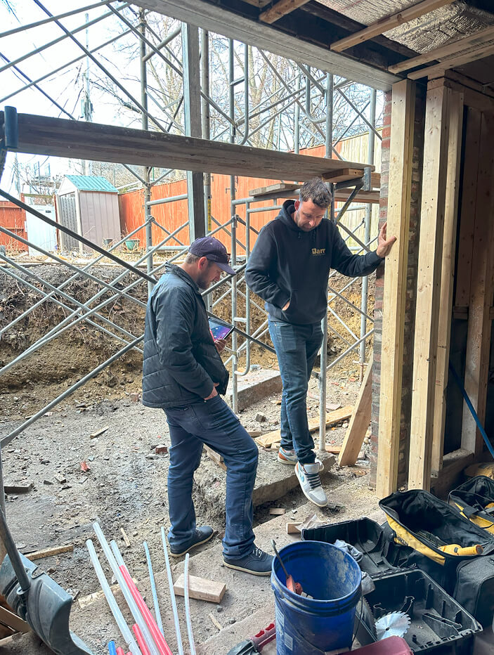 Builder Gareth Barr overseeing the installation of new Marvin windows, part of the ongoing work on the historic brownstone renovation, with views of the future backyard.