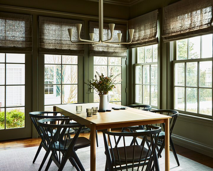 Dining room in Concord home featuring dark green walls, oak dining table, Danish-inspired chairs, and abundant natural window light.