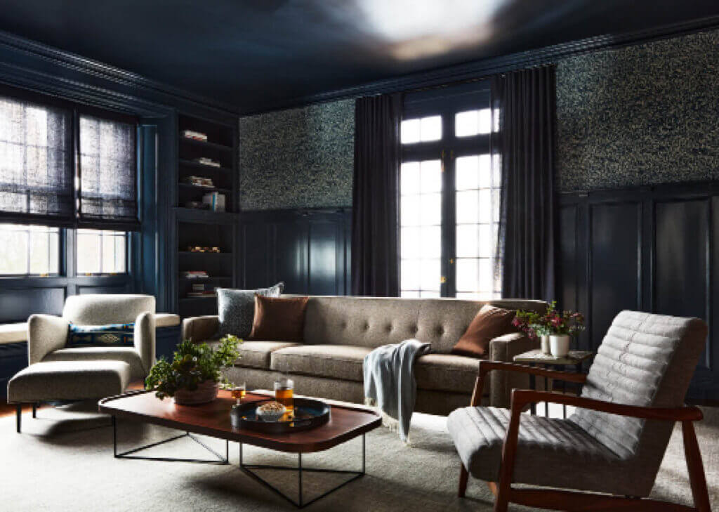 A dark blue room with original millwork, navy wainscot, a window seat, navy Roman shades, mid-century furniture, and drapery panels over French doors.