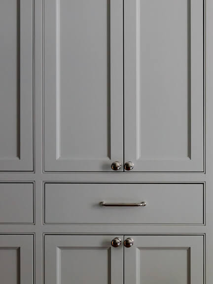 Light grey custom cabinets with polished nickel hardware, hand-finished in New England, featuring simple knobs and drawer pulls in a traditional style.