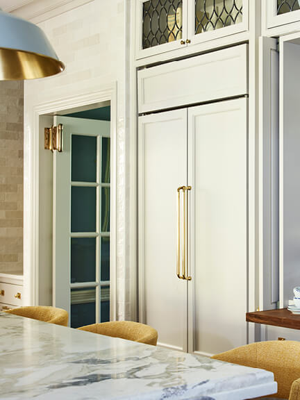 Panel-ready Sub-Zero refrigerator with light grey doors and hand-finished brass hardware, crafted by a company in New England.