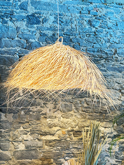 Visit Montreal in the Winter to see a straw pendant light, reminiscent of a beach hat, set against a historic stone wall at Maison Pepin.