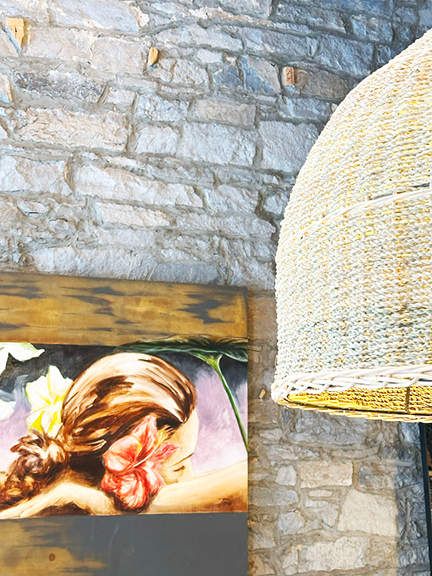 A natural woven pendant light with contemporary art in the background, set against a historic stone wall at Maison Pepin in Old Montreal.
