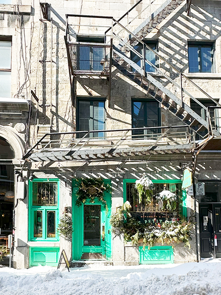 Visit Montreal in the Winter | Bright green storefront with painted windows and doors, set against light beige stone and fresh snow.