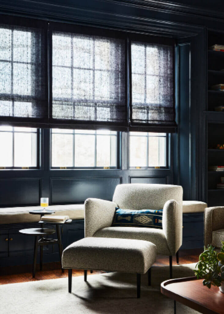Dark blue media room design with mid-century-inspired furniture, a boucle chair and ottoman, a walnut coffee table, and linen Roman shades at the window seat.