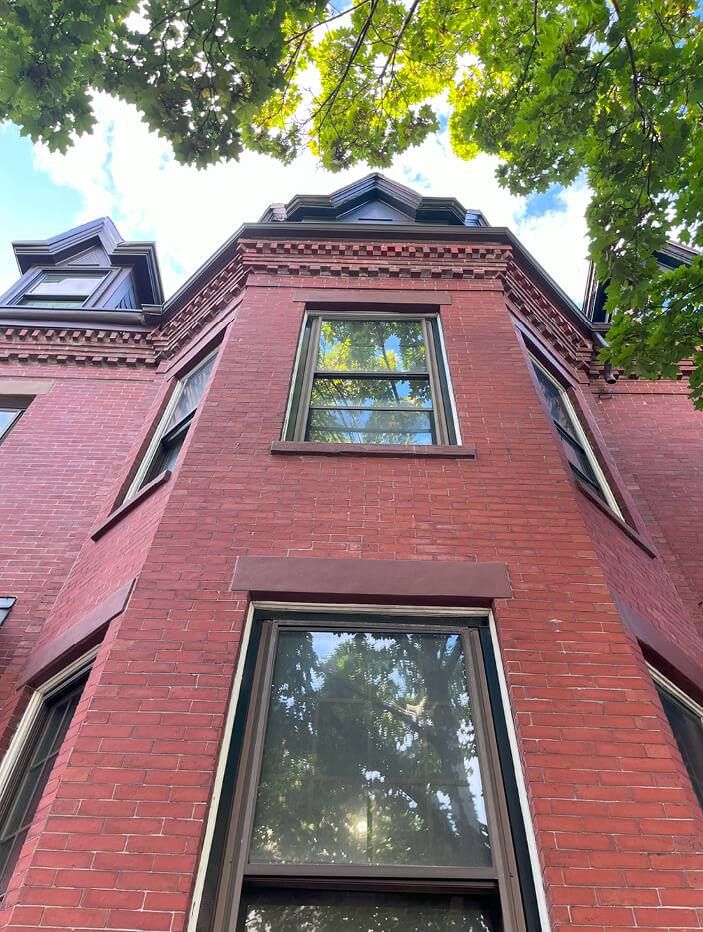 Boston brownstone renovation with the original brick facade and architectural details preserved while replacing the windows at the top level of the building.
