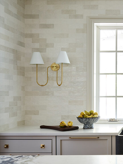 Off-white custom kitchen cabinets with artisan off-white backsplash tile and a brass Urban Electric double beaded wall sconce in a traditional kitchen design.