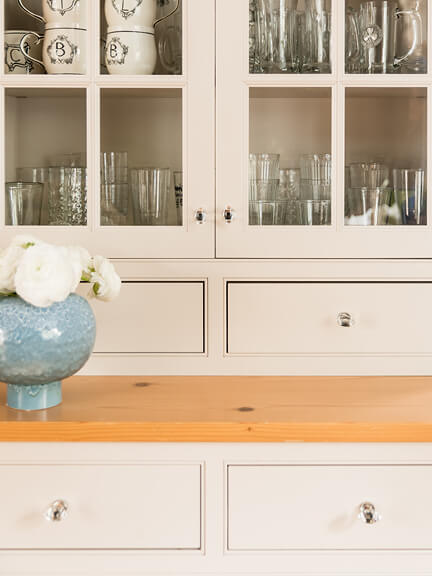 Classic New England kitchen with off-white framed cabinets, beaded detail, slab drawers, glass doors, and glass hardware.