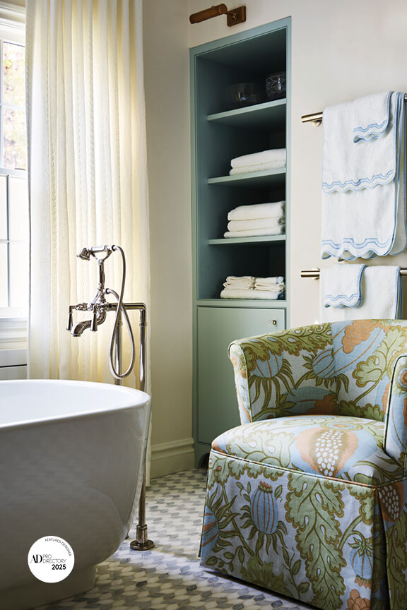 Traditional bathroom with blue cabinets, Newport Brass fixtures, and a slipper chair upholstered in Christopher Farr fabric