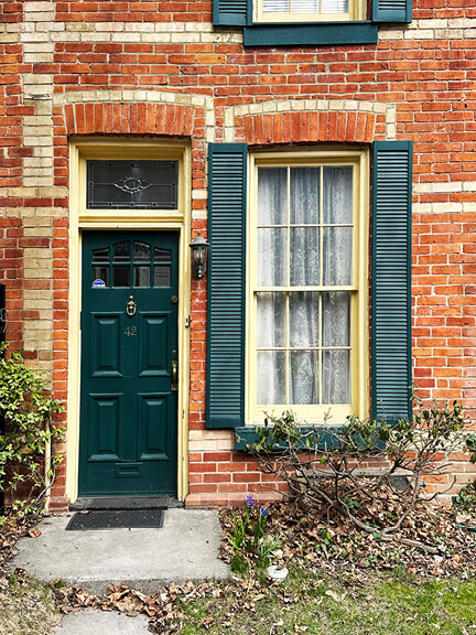 Interior-designer-historic-homes captures dark green door with yellow trim on a historic brick home in Toronto.