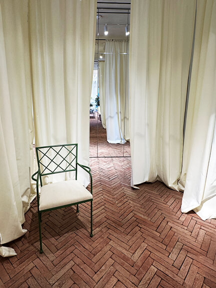 Herringbone floor, white drapery, and iron furniture inside the Jacquemus store in West Hollywood, blending softness with structure.
