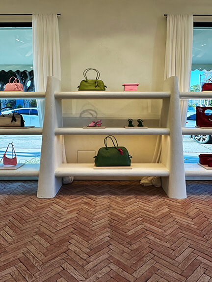 Jacquemus retail interior in LA with terracotta herringbone flooring and custom shelving in a soft, sculptural layout.