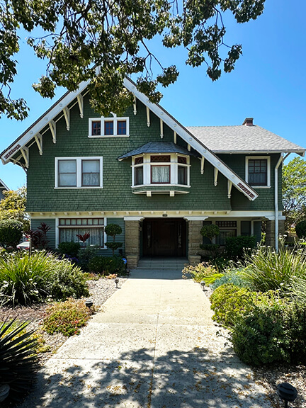 Craftsman-style historic home in Los Angeles with hunter green siding, deep roof eaves, and early 20th-century architectural details.