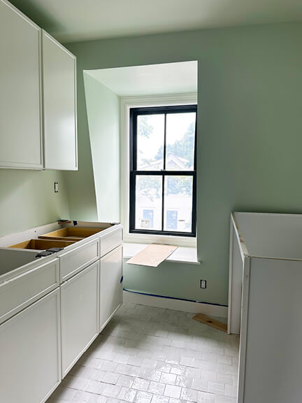 Light green walls and white cabinets define this soft, airy laundry room in a historic Boston brownstone