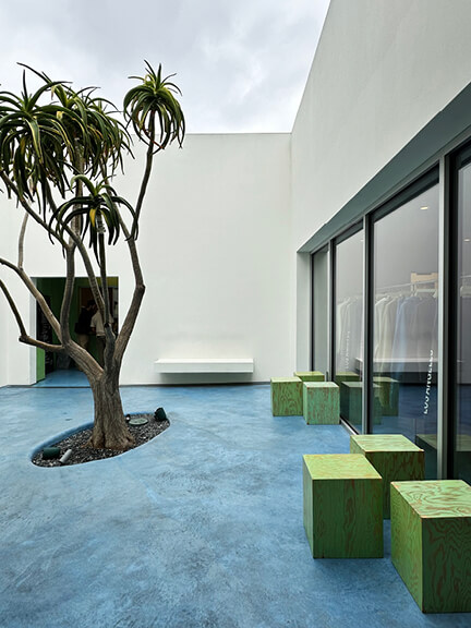 Modern courtyard at Madhappy Los Angeles with blue flooring, white stucco walls, and a clean, sculptural retail design.
