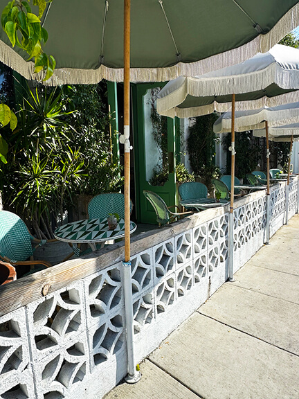 Outdoor seating at The Butcher’s Daughter in LA with green fringe umbrellas, offering a playful, shaded spot for casual dining.