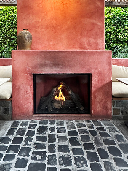 Pink plaster fireplace with tumbled stone flooring in a West Hollywood restaurant, blending softness with rustic materials.