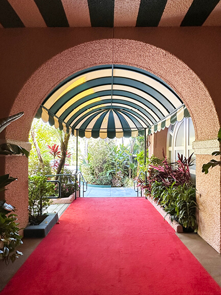 Historic architecture in Los Angeles shown in a pink stucco building with a green striped awning and red carpet at the Beverly Hills Hotel.