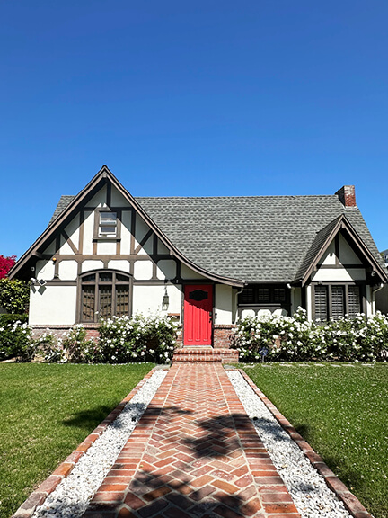 A half-timber storybook-style home in Los Angeles with a bright red door and herringbone brick walkway leading to the entrance.