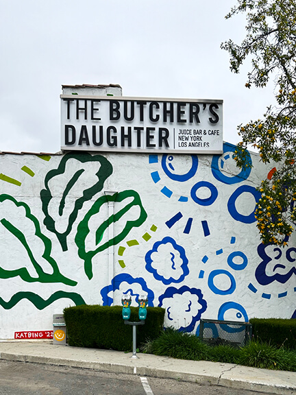 Exterior of The Butcher’s Daughter in West Hollywood featuring graffiti-style decor and bold curb appeal. Shop and Dine LA.