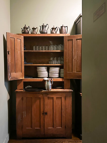 Vintage cupboard with silver serveware at A.O.C. Brentwood, styled by Nickey Kehoe with collected details and classic charm.