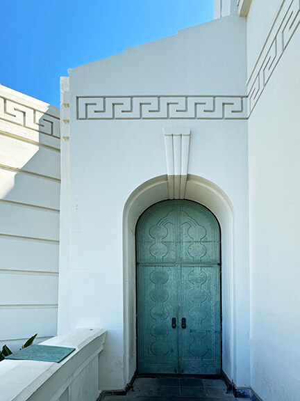 Aged metal doors with green patina set into white architecture at Griffith Observatory—detailed historic design in Los Angeles.