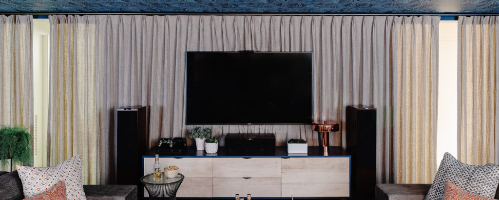 Floor-to-ceiling beige linen drapery panels soften the basement TV room and conceal two doorways leading to the playroom