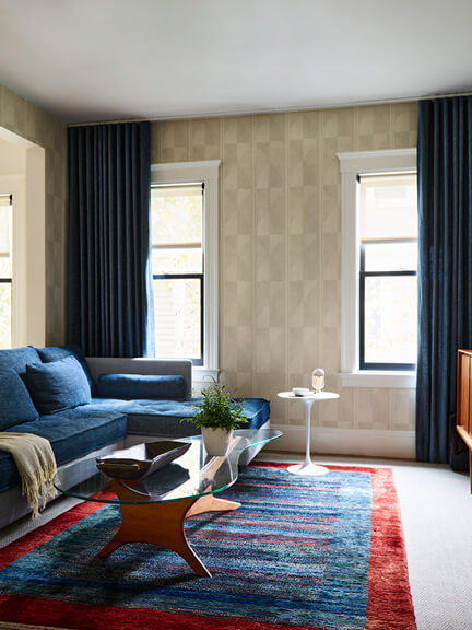 Custom window treatments with dark blue linen drapery panels on a ceiling track in a historic Brookline home with vintage rug and upholstery