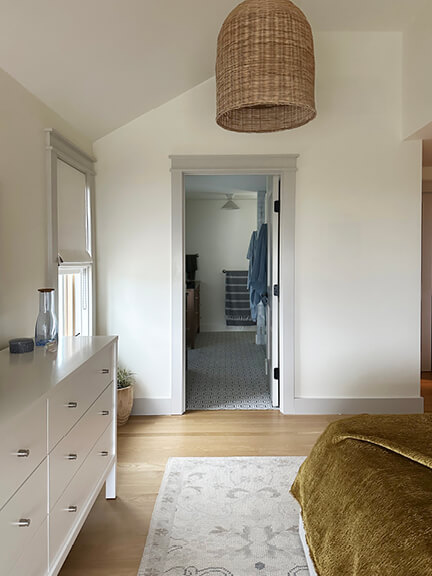 Primary bedroom with grey window trim, white walls, and rattan pendants.