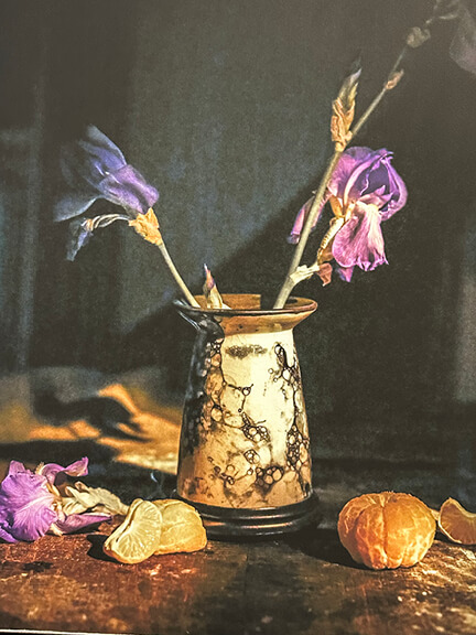 Art in interior design featuring Curtis Speer’s still life photograph of a vintage vase with flowers and an orange on dark background