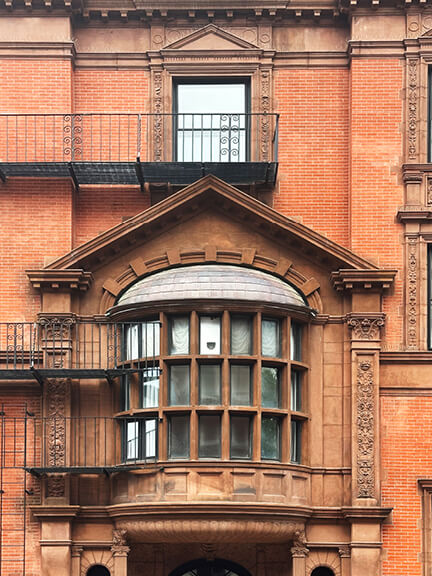 Brownstone oriel window with classical pediment on a red brick Boston townhouse, a detail reflecting historic home design in Boston.