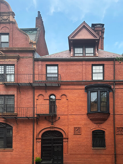 Asymmetrical brick townhouse with arched windows, small bay windows, and a carved dormer—uncommon among Boston’s historic façades.