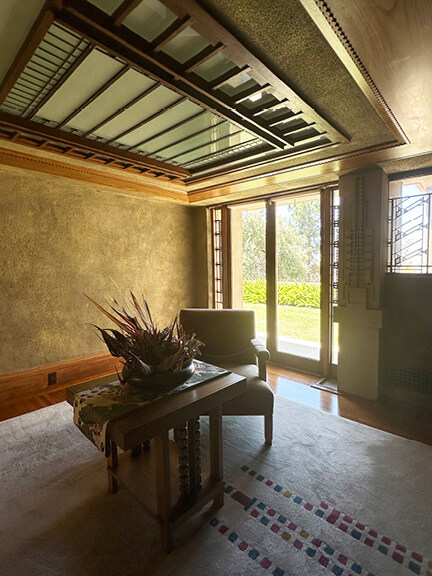 Desk, chair, custom windows, and unique rug beneath ceiling trellis at Hollyhock House, part of postmodern architecture Los Angeles tour
