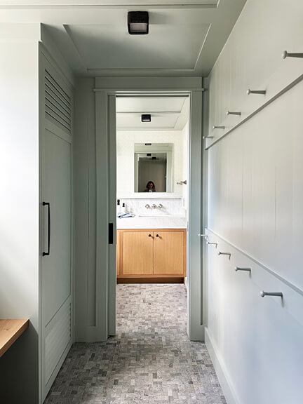 Light blue mudroom with wall hooks and storage in a new construction beach house.