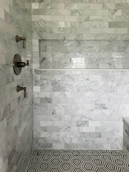 Marble shower with wall tile and satin brass fixtures in a coastal interior design.