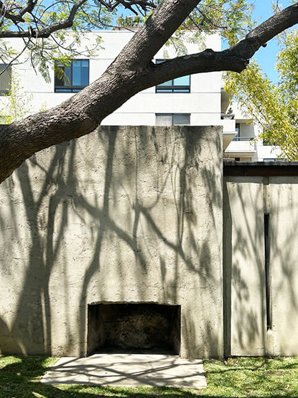 Concrete outdoor fireplace in Schindler House courtyard, framed by stucco walls and open-air layout
