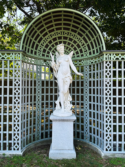 French inspired garden with a wooden trellis crowned by a sphere over a marble sculpture in the Rhode Island landscape.