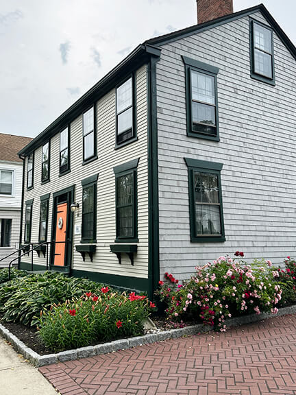 Colonial-style home with wood shingles, green trim, and orange door in Bristol, RI, photographed by New England historic home designer