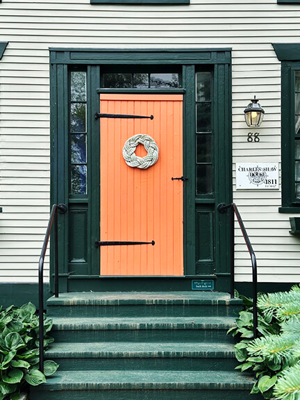 Close-up of orange colonial front door with iron hinges and green trim on 1811 home in Bristol, Rhode Island