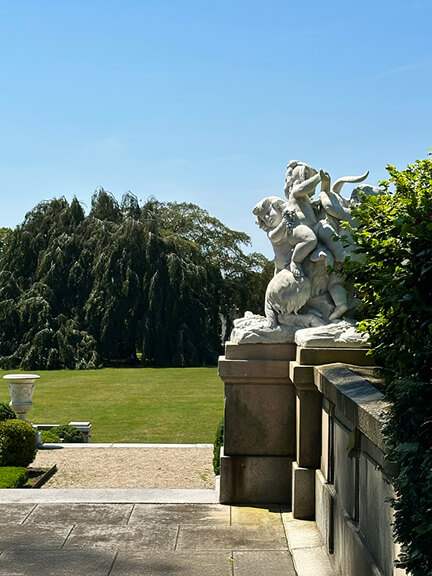 The Elms Newport Mansion side patio view looking toward the great tree and marble statues across the historic estate grounds.