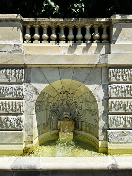 Classic French garden design with marble fountain featuring a sculpted fish at the historic estate.