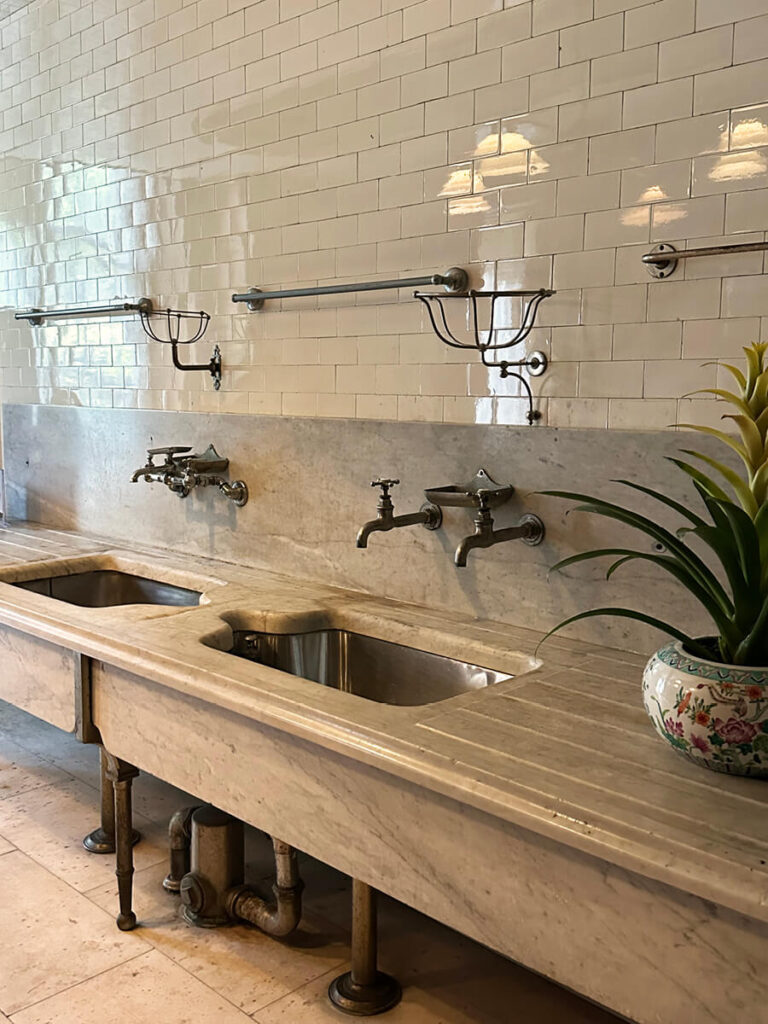 Gilded Age kitchen at The Elms in Newport with tiled walls, marble counters, wall-mounted faucets, and aged hardware, exemplifying Gilded Age Interior Design.